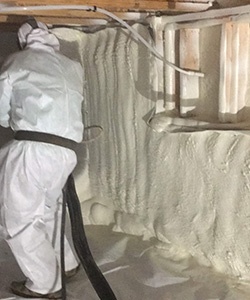 Worker installing spray foam in a crawl space.