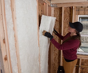 Worker installing fiberglass insulation in a wall.