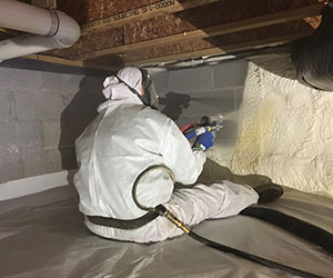 Worker installing insulation in a crawl space.