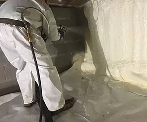 Worker installing spray foam in a crawl space
