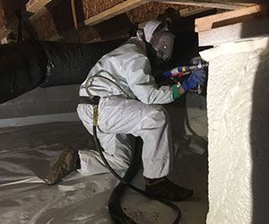 Worker installing insulation in a crawl space.