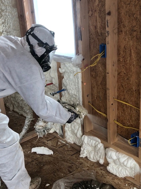 Worker installing spray foam insulation in a tiny home wall.