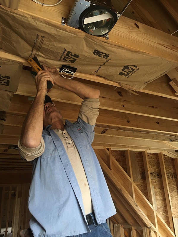 Worker installing fiberglass insulation in a ceiling.