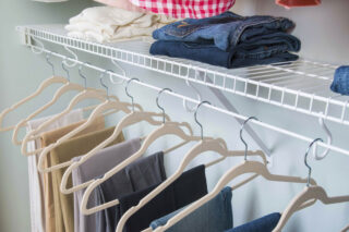 Closeup of organized clothing on hangers and on white wire shelf in closet.