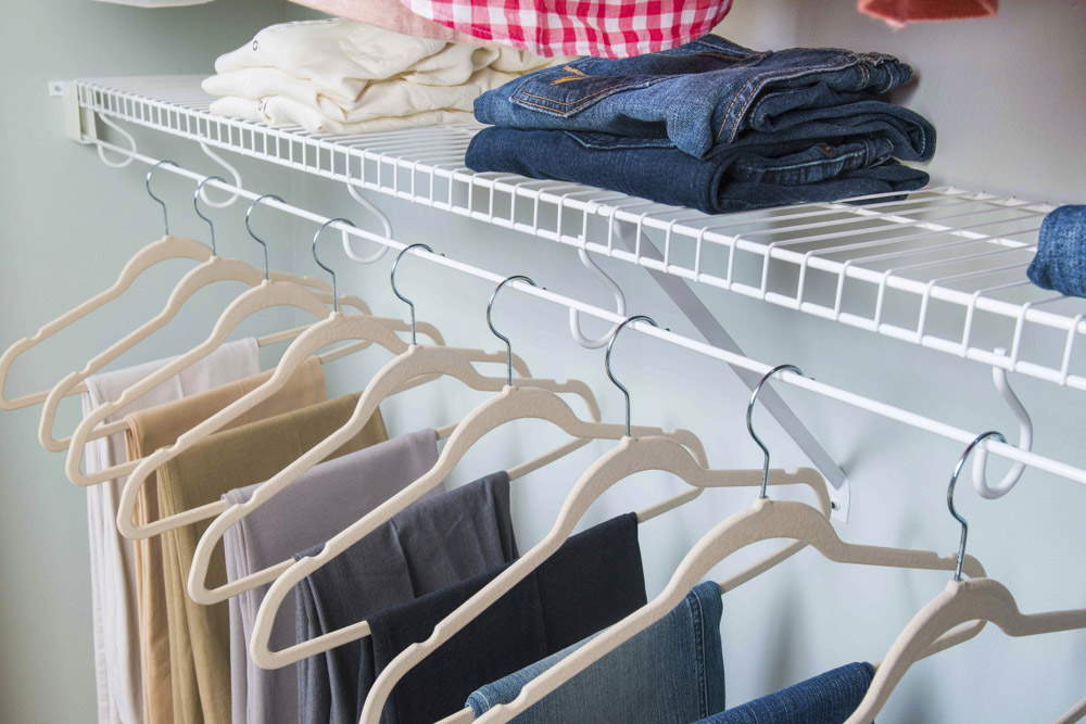 Closeup of organized clothing on hangers and on white wire shelf in closet
