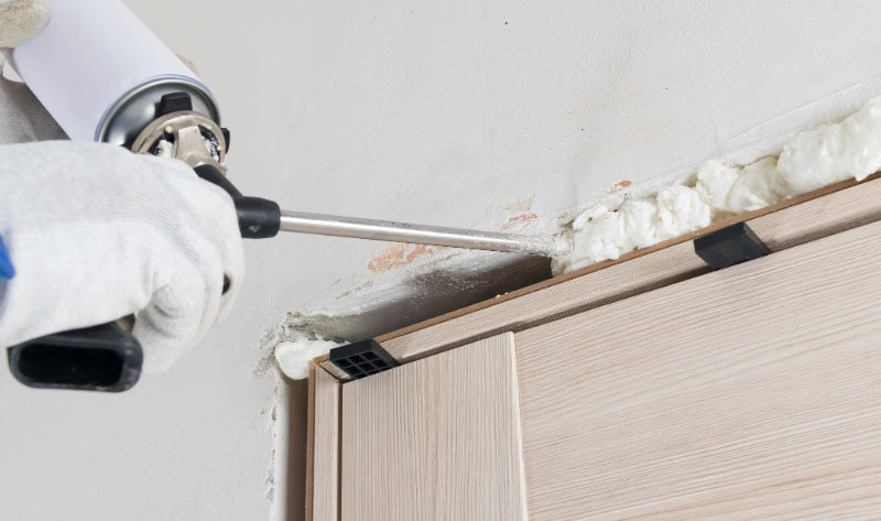 Contractor applying spray foam insulation to seal air leaks around a door frame.