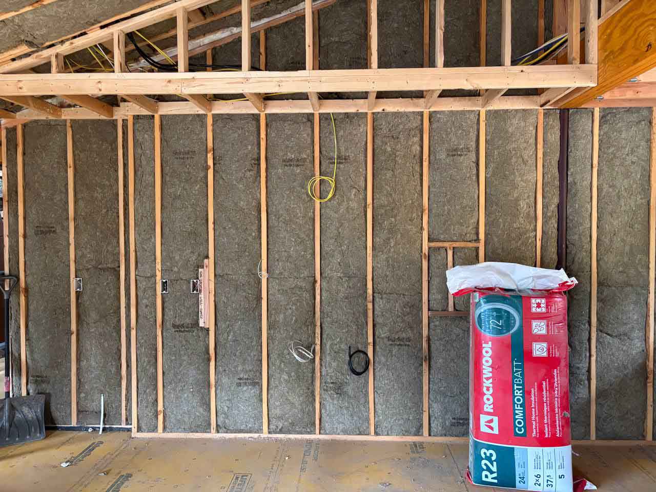 Construction site view showing Rockwool ComfortBatt R23 insulation installed in walls alongside the original product packaging.