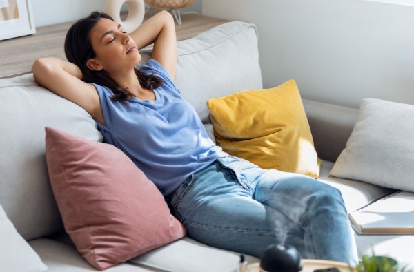 Beautiful woman relaxing on a coach while essential oil aroma diffuser humidifier the air in living room at home.