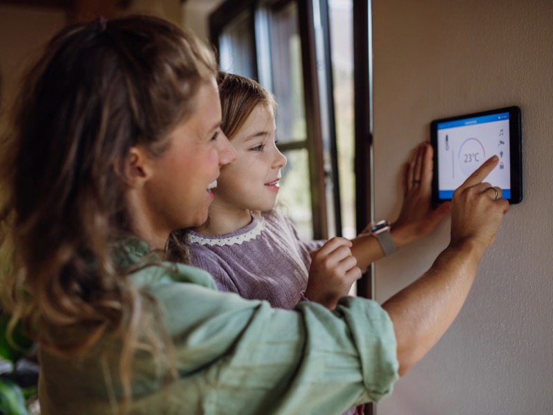 Girl helping mother to adjust, lower heating temperature on thermostat. Concept of sustainable, efficient, and smart technology in home heating and thermostats.