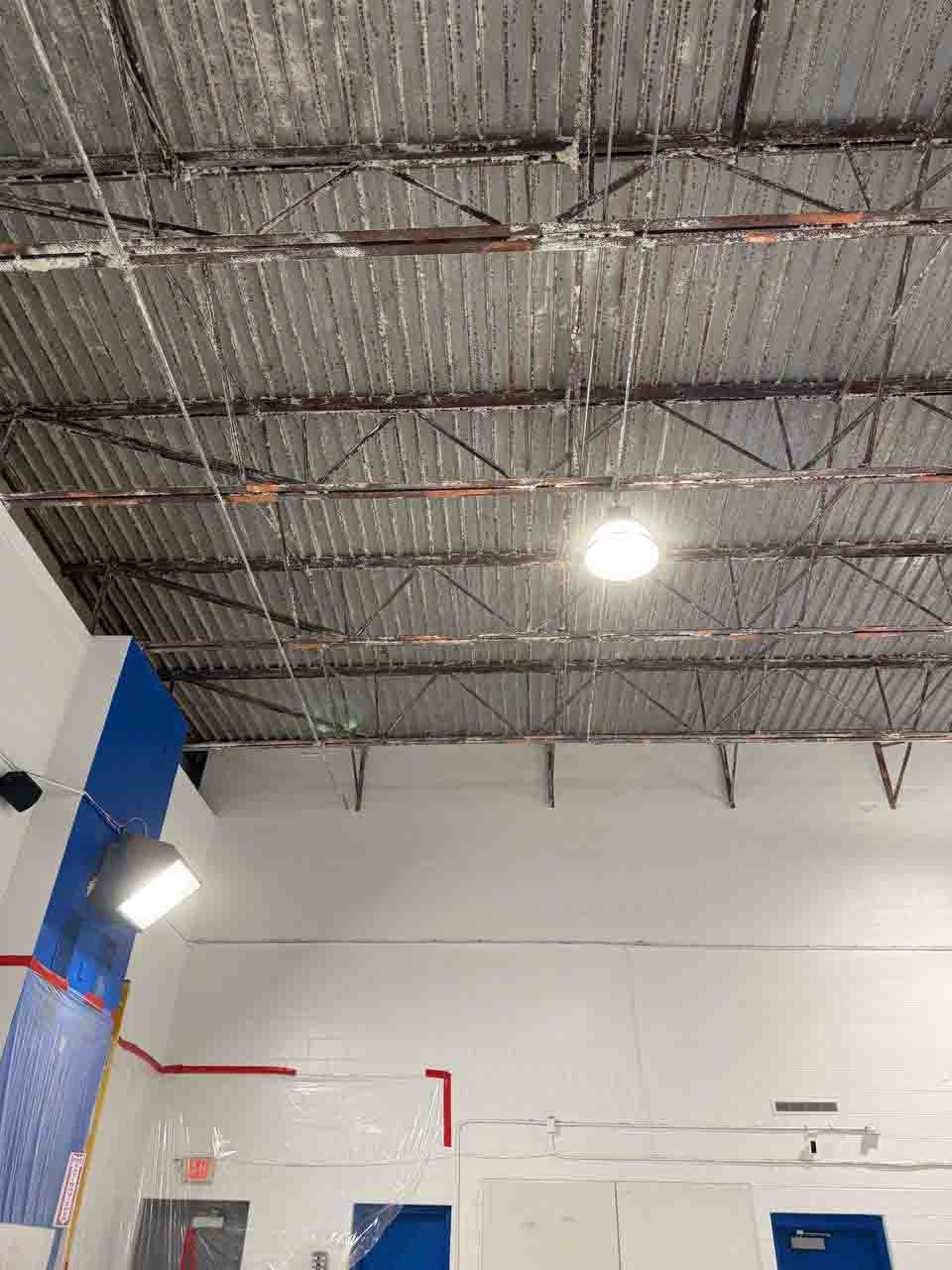 Uninsulated corrugated metal ceiling with steel trusses in a commercial gym before insulation work.