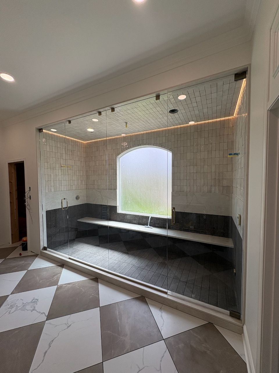 Custom frameless glass shower with arched window and marble bench installation in Kansas City by The Hayes Company.