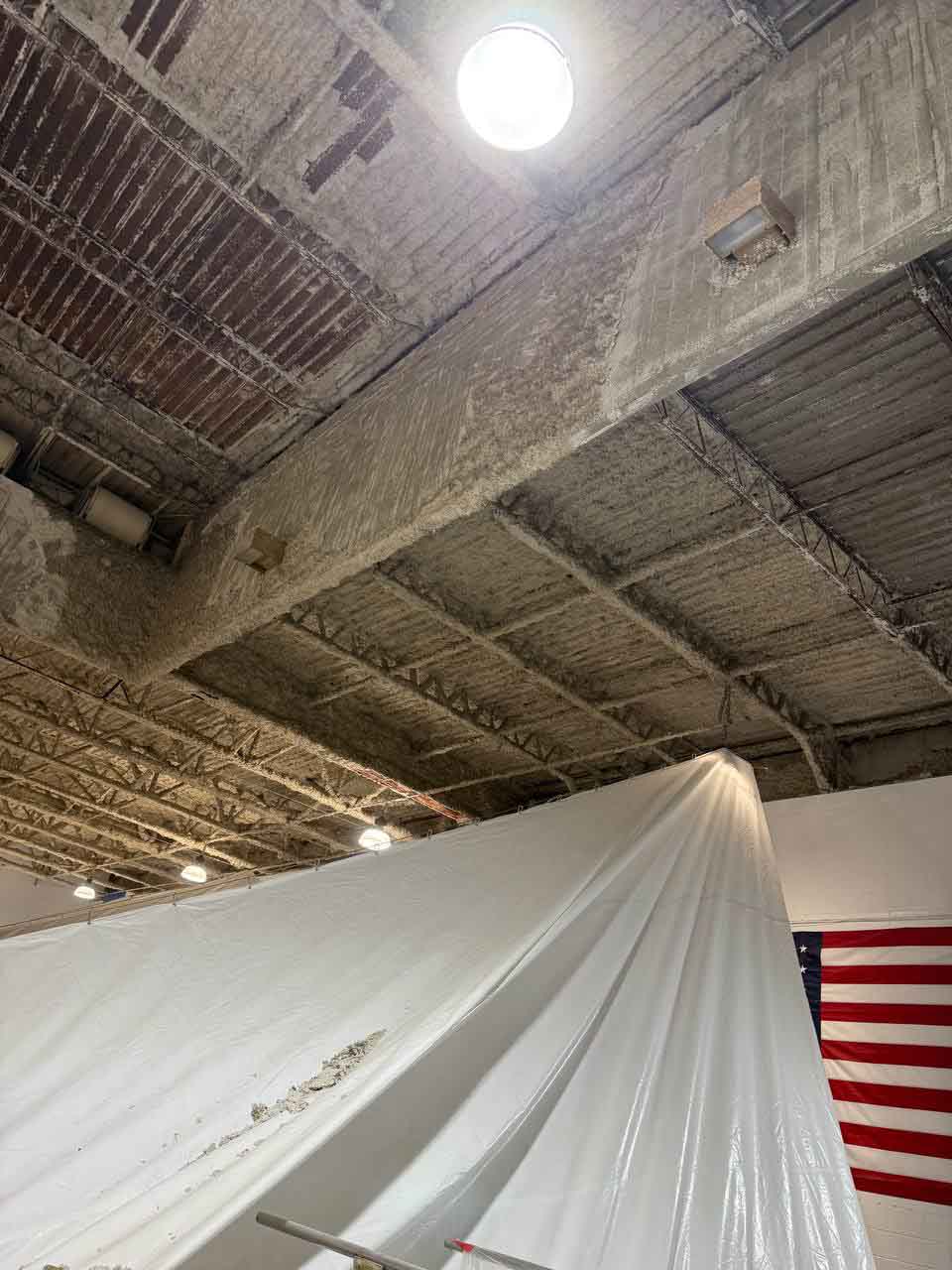 Spray foam insulated commercial ceiling with white drop cloth and American flag visible below.
