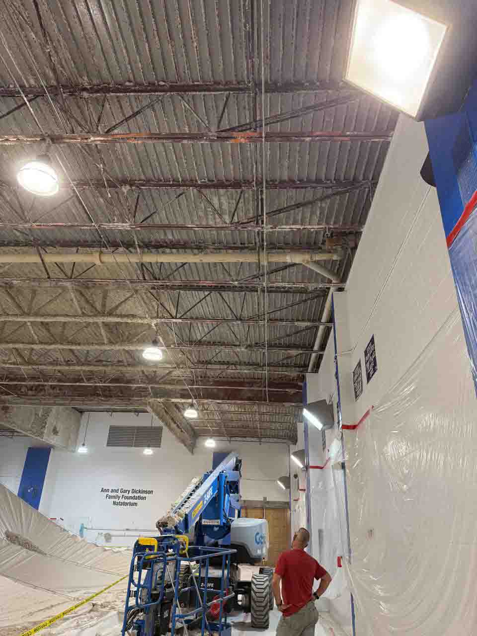 Worker surveying uninsulated natatorium ceiling from below with boom lift ready for spray foam application.