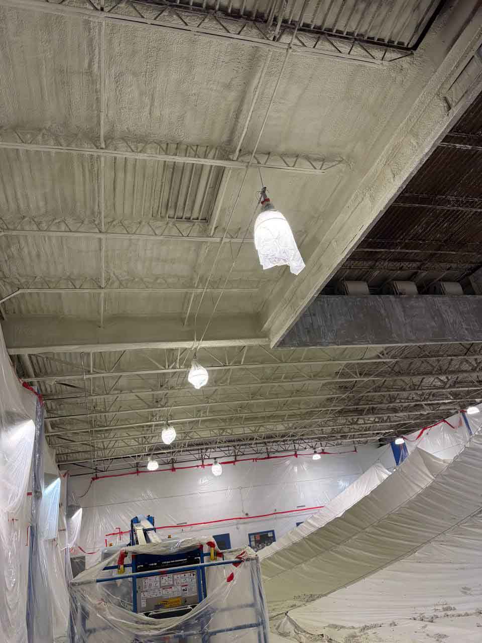 Finished spray foam insulation on natatorium ceiling with boom lift and spray equipment still on site.