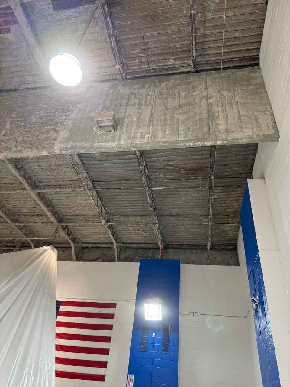 Uninsulated corrugated metal ceiling section in natatorium with American flag and blue accent wall below.