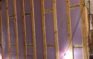 Close-up view of 1.5-inch pink rigid foamboard insulation fitted into open wall cavities between wood studs during new construction at 74 Broadway Kansas City. Close-up view of 1.5-inch pink rigid foamboard insulation fitted into open wall cavities between wood studs during new construction at 74 Broadway Kansas City.