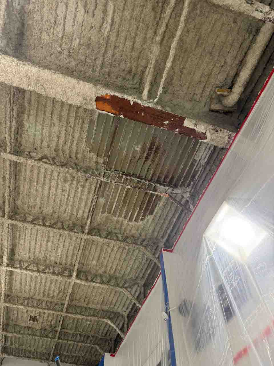 Spray foam insulation partially applied to a commercial ceiling with plastic containment barrier below.