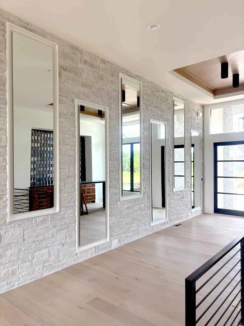 Row of framed full-length mirrors installed on stone accent wall in foyer stairway, Kansas City.