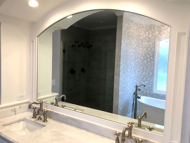 Large arched frameless mirror installed above double vanity sinks in Kansas City bathroom by The Hayes Company.