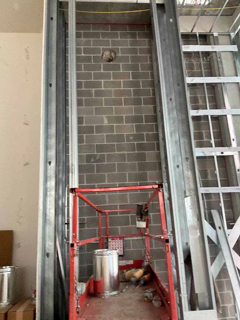 Vent opening in a masonry block wall above a scissor lift staged with vent pipe for a Montigo Prodigy 2 gas fireplace install at Berkley Riverfront in Kansas City, MO.
