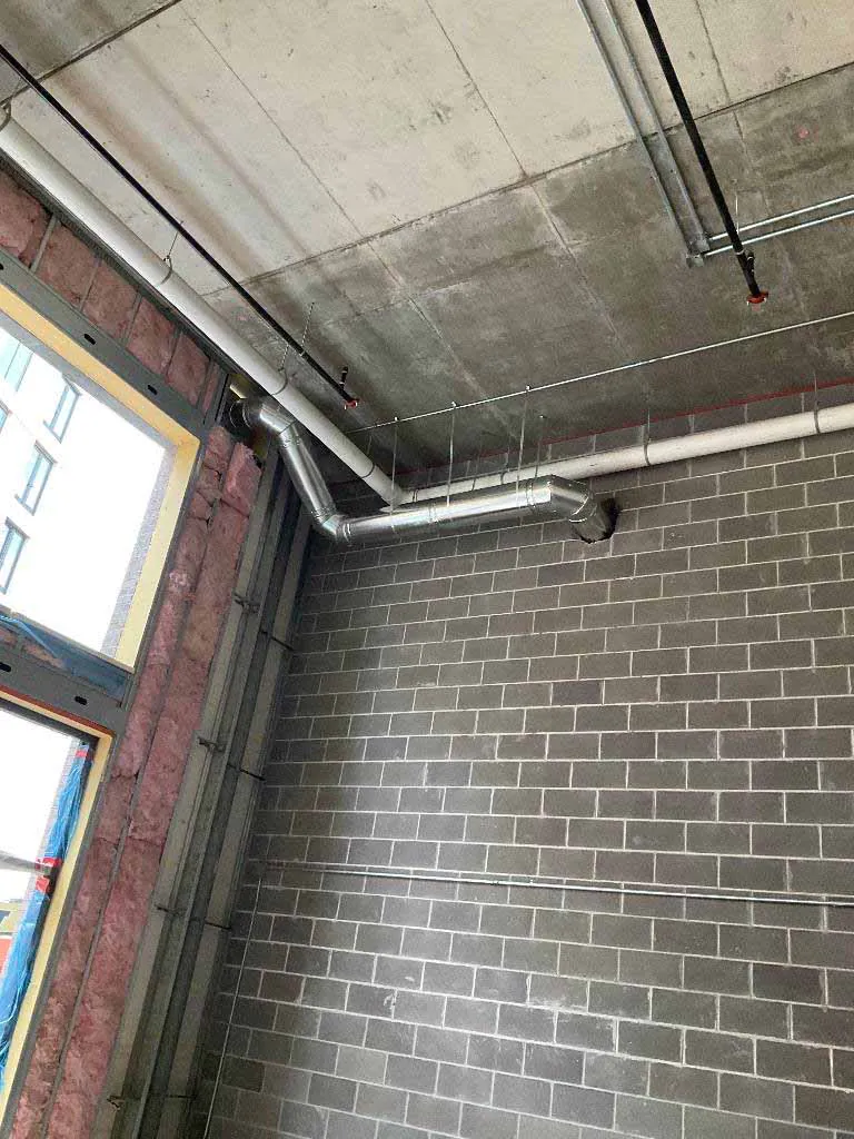 Gas fireplace vent pipe routed along an exposed concrete ceiling between masonry wall penetrations for a Montigo Prodigy 2 install at Berkley Riverfront in Kansas City, MO.