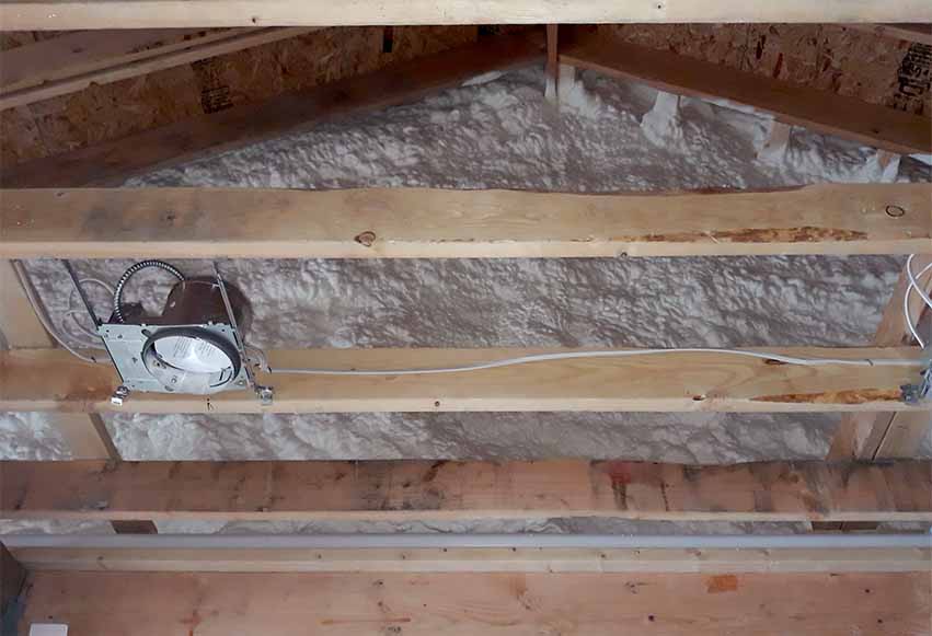 Hayes Insulation KC open-cell spray foam insulation sprayed on the underside of the roof deck above open ceiling joists and a recessed light housing in Kansas City, MO.