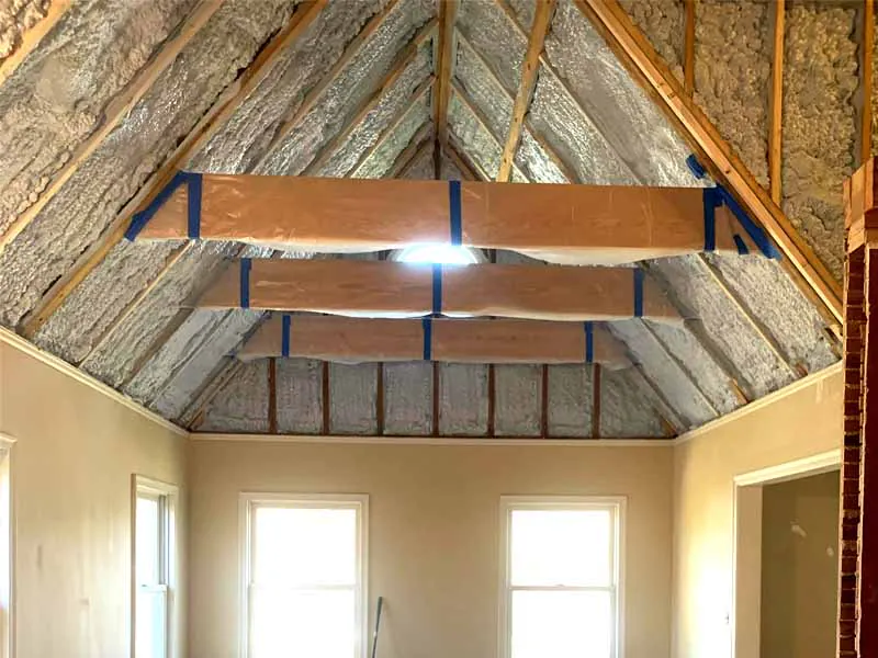 Hayes Insulation KC open-cell spray foam insulation applied to the roof rafters of a vaulted ceiling conversion, with exposed beams masked for protection, in Kansas City, MO.