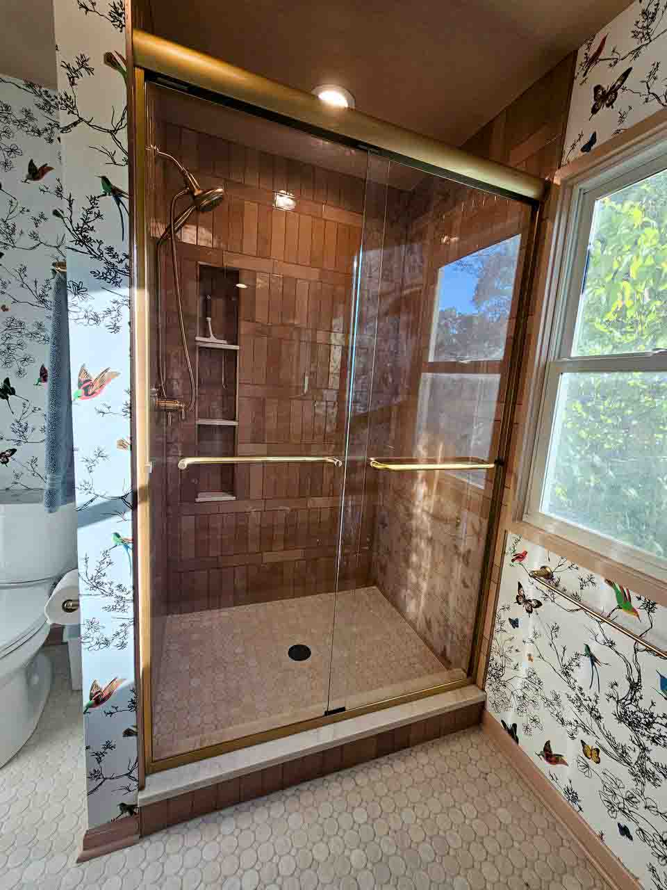 Brushed bronze sliding glass shower door with matching towel bars, installed by The Hayes Company in a Leawood, KS bathroom.