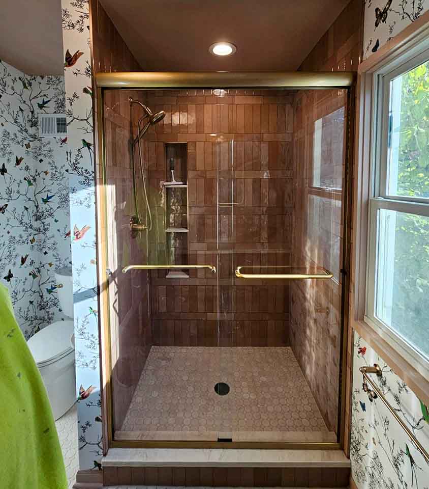 Front view of a brushed bronze bypass shower door enclosing a terracotta-tiled walk-in shower with a recessed niche in Leawood, KS.