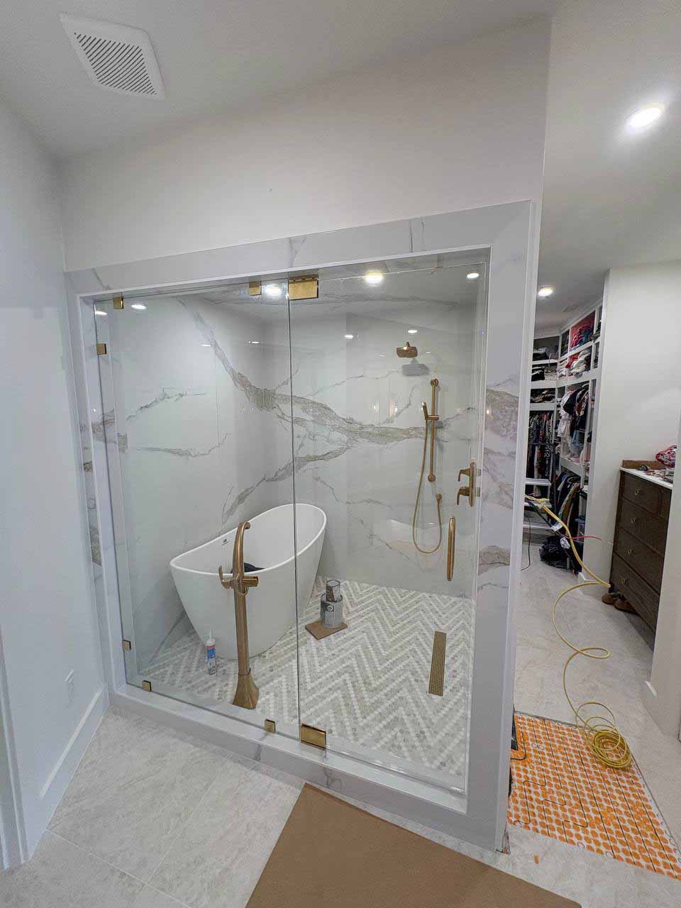 Floor-to-ceiling frameless glass enclosure with brushed gold hardware around a freestanding tub and marble-look shower in Kansas City.