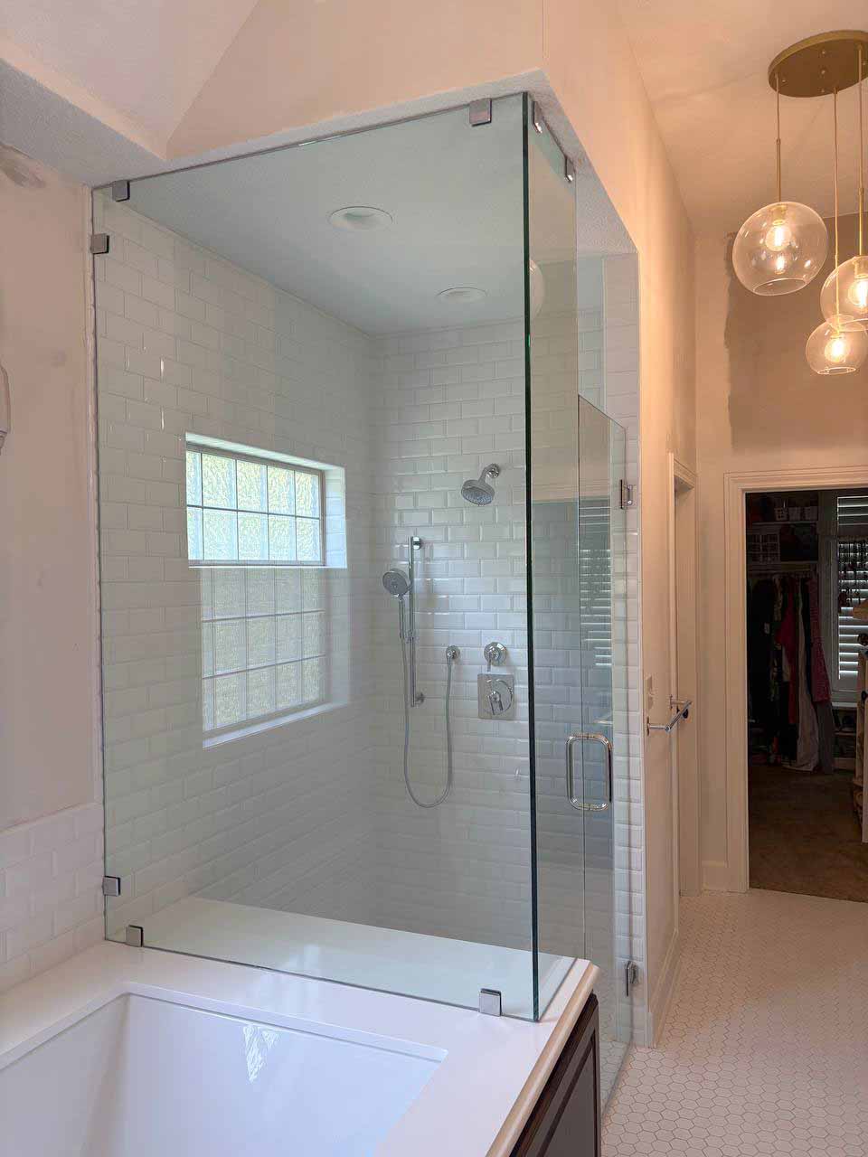 Frameless corner glass shower enclosure with chrome clips mounted on a tub deck beside white beveled subway tile in Kansas City.