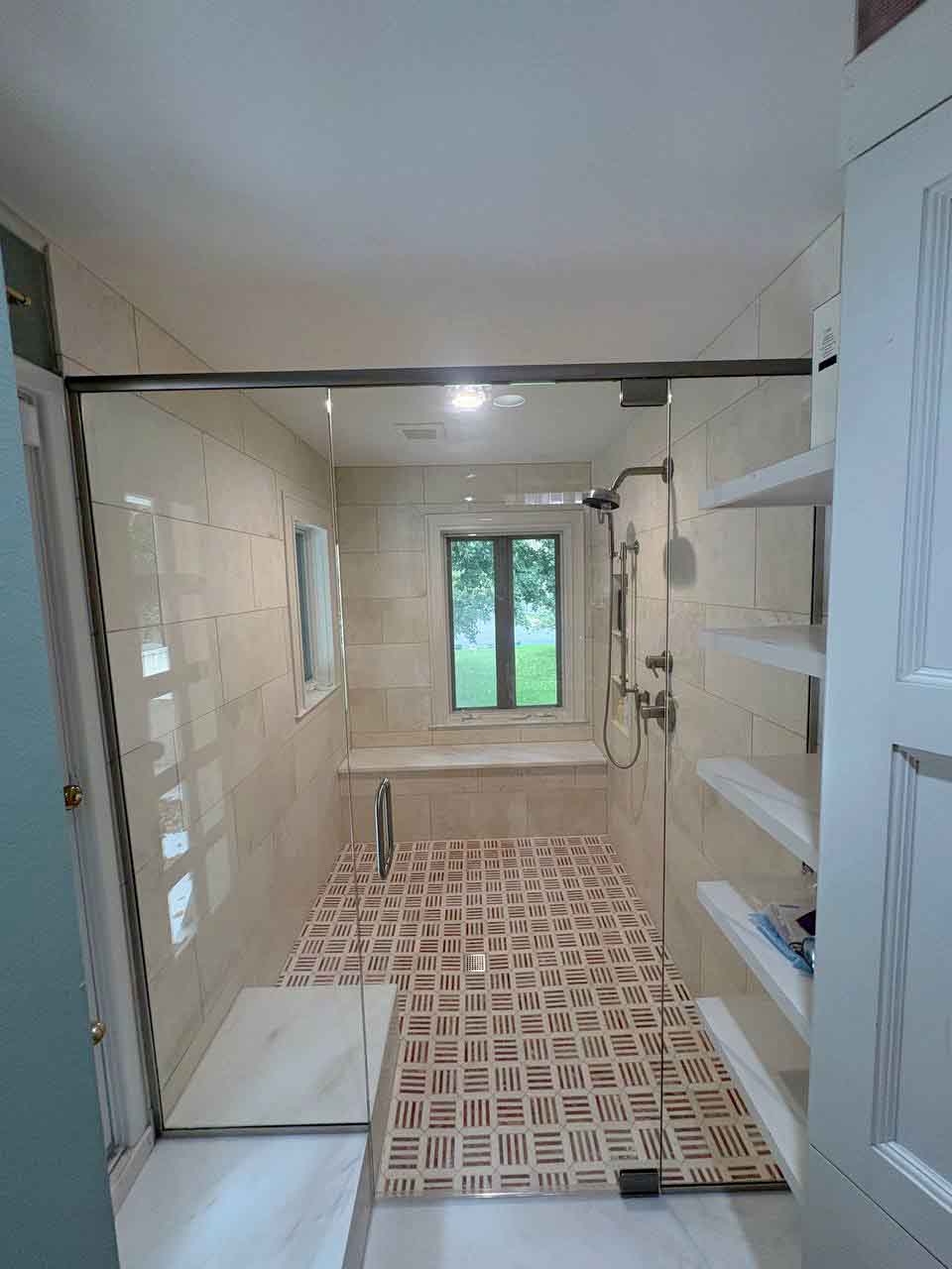 Frameless hinged glass shower enclosure with a brushed nickel header bar opening onto a walk-in shower with a bench and window in Kansas City.